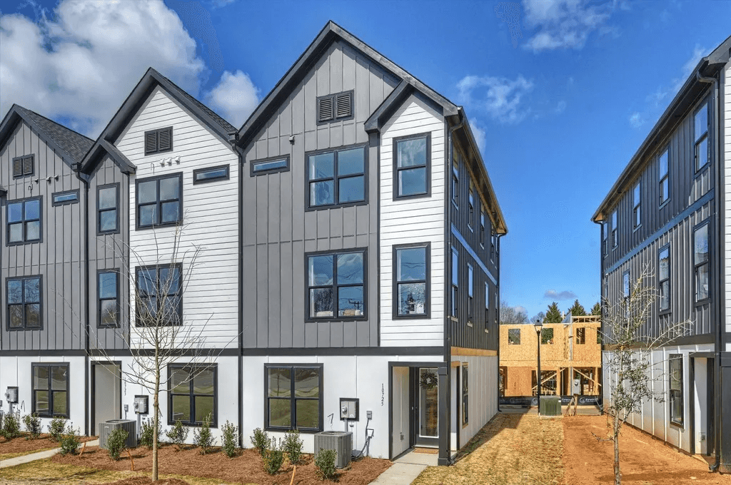 A row of three-storey townhomes in charcoal and white siding with black window frames, gabled roofs and attached garages, with construction continuing beyond the row.